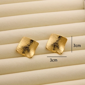 Detail showing 3cm square gold stud earrings with a textured hammered metal surface