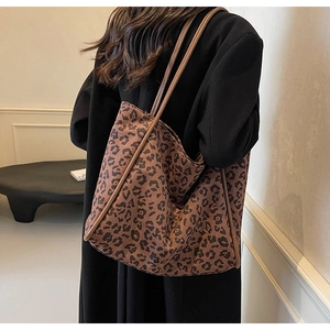 Close-up of leopard print tote bag with brown straps worn by a model in a black coat