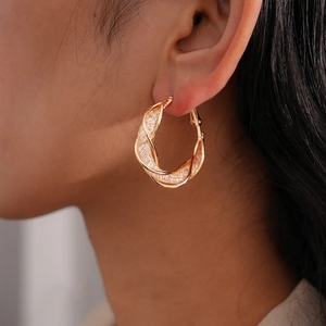 Detailed close-up of large twisted gold-tone hoop earrings on a model with metallic texture
