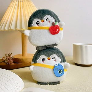 Cute grey penguin plush coin purse with camera and apple charms in a cozy desk setting