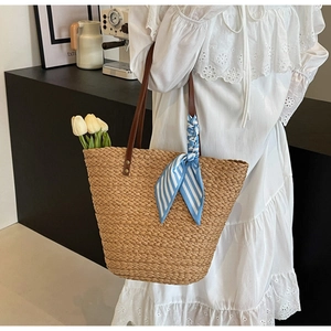 Detail of straw tote bag with brown leather handles and a blue striped silk scarf