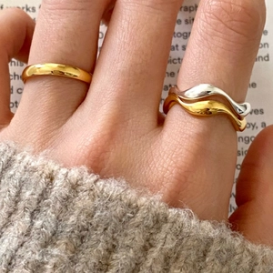 Close-up of stacked gold and silver wave rings with a sleek minimalist band on fingers