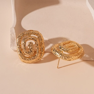 Detailed macro view of gold hammered square spiral earrings on a beige textured stone