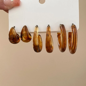 Detailed set of three amber acrylic C-shaped hoop earrings on a white display card