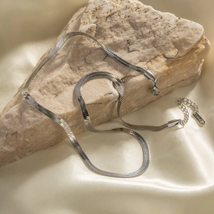 Sleek silver stainless steel flat snake chain necklace on stone with silk background