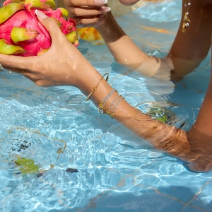 Golden balloon initial charm bracelet with zircon stones worn by model in a pool setting