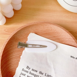 Close-up of a white seamless duckbill hair clip on vintage paper in a wooden bowl