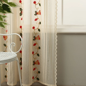 Detail of Christmas bell embroidery on cream lace curtain with festive holly leaf patterns