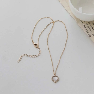 Detail of a golden heart necklace with cat-eye stone and white diamonds on grey background