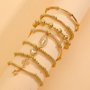 Detail of layered gold bracelet set featuring heart, cross, and star charms on display