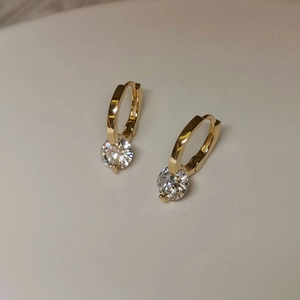 Detail of gold hoop earrings featuring sparkling round zircons on a beige background
