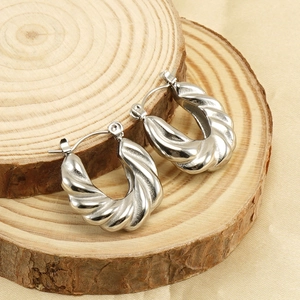 Détail de créoles torsadées en argent poli sur un support en bois de style rustique