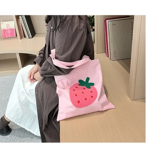 Pink canvas tote bag featuring 3D strawberry embroidery in a cozy library setting