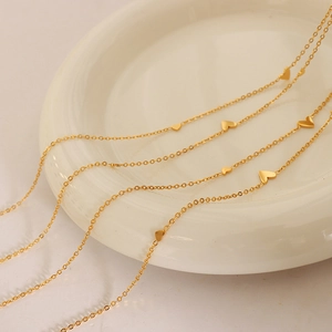 Minimalist 18K gold plated titanium necklace with small heart charms on a white plate