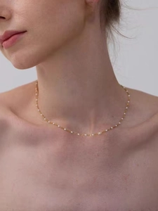 Close-up of a minimalist golden choker necklace with white enamel beads on a female neck