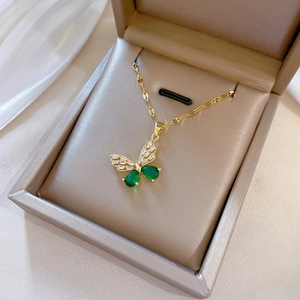 Macro detail of gold butterfly necklace with green gems and diamonds in a gift box
