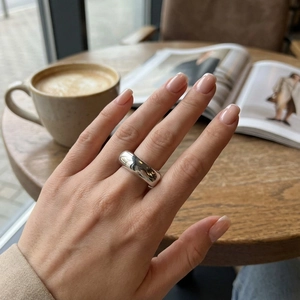 Polished silver stainless steel thick ring worn by a model in a refined cafe setting