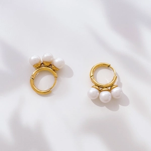 Detail of gold pearl hoop earrings with elegant fringe design on white fabric