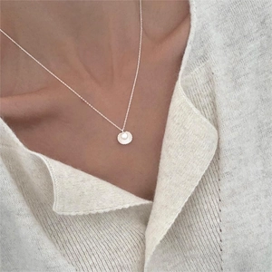 Close-up of a silver shell pendant necklace with a round pearl on a white knit sweater