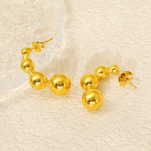 Detailed view of gold ball-shaped C-style earrings with polished mirror finish on neutral texture