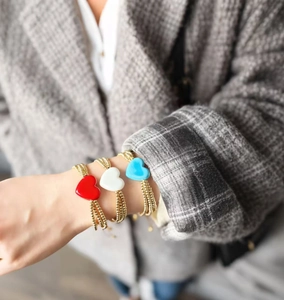 Detalle de pulseras multihilo de cuentas de cobre doradas con dijes de corazón de vidrio.