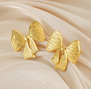Gros plan détaillé de boucles d'oreilles nœuds dorés sur fond de soie couleur champagne