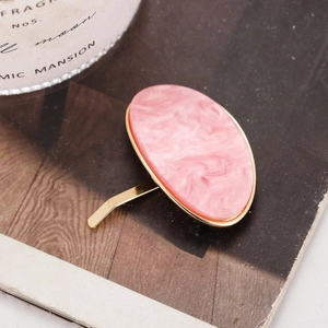 Pink marble oval ponytail hook with gold metal frame on a rustic wooden surface