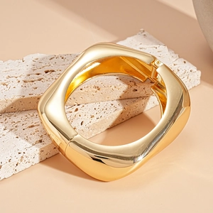 Dettaglio di un bracciale rigido dorato quadrato con finitura lucida e cerniera