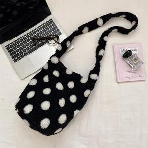Polka dot plush shoulder bag styled with laptop and magazine on white fabric background
