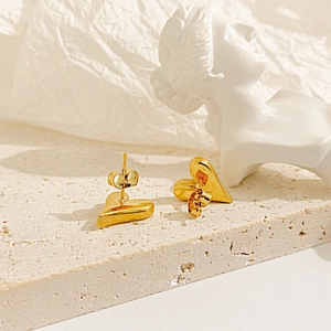 Macro detail of 18k gold plated heart stud earrings on elegant stone pedestal