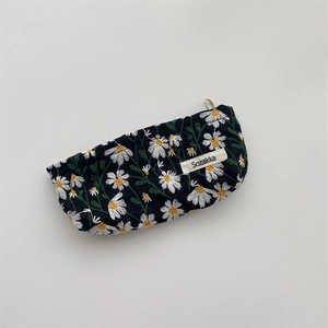 Detail of white daisy embroidery on black fabric pouch with woven brand tag and zipper