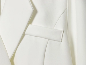 Detailed close-up of white blazer fabric texture with lapel and flap pocket stitching