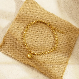 Golden bead chain bracelet with round spherical charm on natural textured burlap background