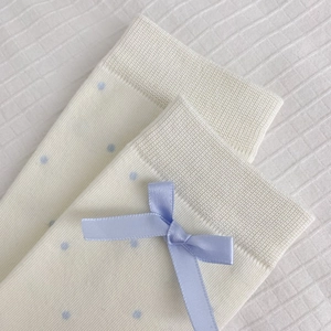 Détail de chaussettes en maille crème avec pois bleus et détail de nœud en satin