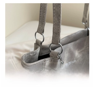 Detail of silver metal buckle and chain on gray tote bag with brand lettering