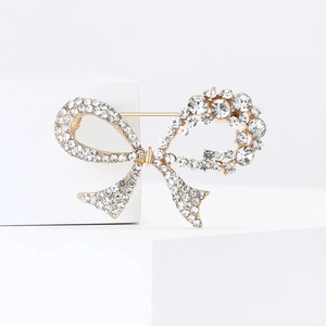 Elegant gold bow brooch featuring sparkling rhinestones on a minimalist white display