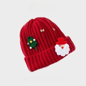 Detailed view of red knitted Christmas beanie with Santa and sparkling bow patches