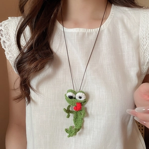 Detail of a handmade crochet frog pendant necklace with red tongue on a lace top