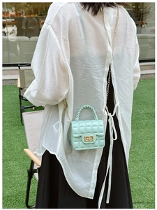 Close-up of mint green quilted jelly bag with gold chain strap on outdoor grass