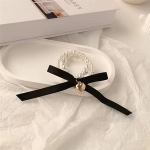 Close-up of pearl beaded bracelet with black satin bow and golden heart charm on tray