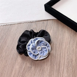 Detail view of large blue satin camellia flower hair tie with white edging on wood