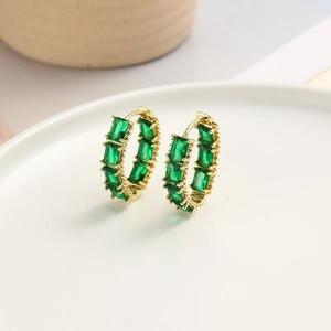 Macro view of gold hoop earrings featuring emerald-cut green zircon in a claw setting