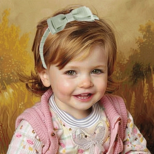 Detail shot of a light green ribbed fabric bow headband worn by a young girl