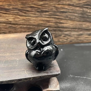 Macro shot of 3.5cm black obsidian owl carving on a textured dark wood base