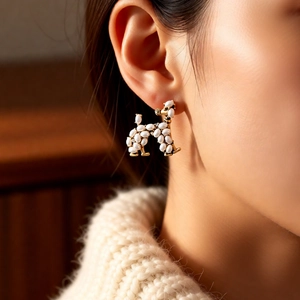 Close-up of a poodle-shaped pearl earring worn on the ear against a warm knit sweater