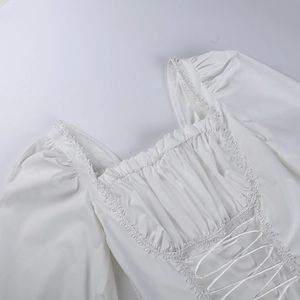 Detalle de blusa blanca con escote cuadrado, mangas abullonadas y cordones frontales