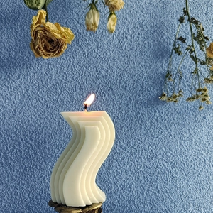 S-vormige geurkaars op bronzen voet met een warme vlam voor een modern interieur