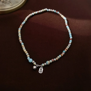 Close-up of beaded necklace with blue natural stone beads and silver auspicious tag