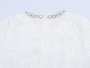 Détail du col d'une robe blanche avec fleurs 3D, strass et fermeture éclair invisible