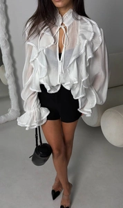 Dettaglio di una camicia in pizzo bianco con volant e maniche a campana dal design chic